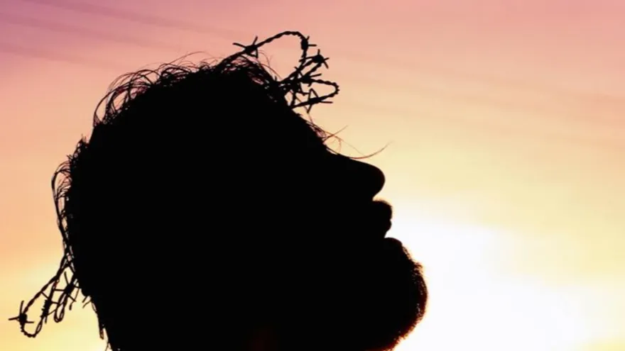 A person in silhouette with head bowed at sunset